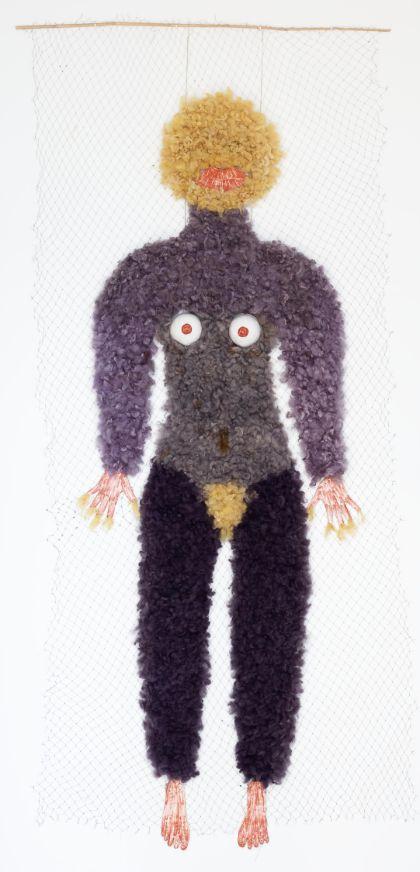 A hanging anthropomorphic figure made of textile-like materials. The figure has a dark purple, fluffy-looking body with arms and legs extended. The head is round, light yellow, and textured.