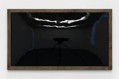 A glossy black rectangle in a dark wooden frame hangs horizontally on a white wall. Its reflective surface faintly mirrors the surrounding space. The artwork is shown from the front.