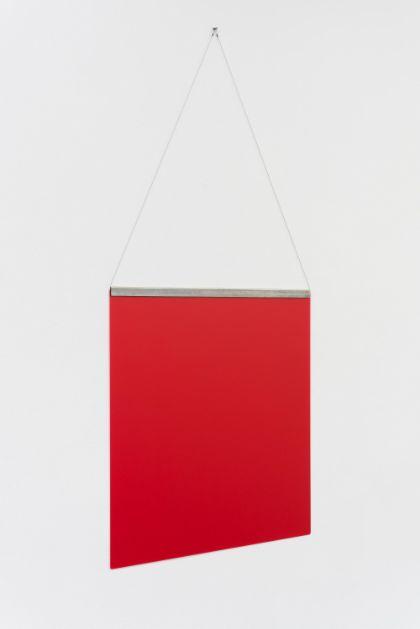 A thin, square red surface hangs on a white wall, attached along its upper edge by taut threads connected to a narrow metal frame. The photograph shows the object from a side perspective.