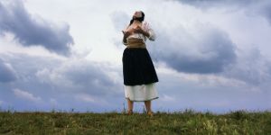 Eine Person mit einem schwarzen Tuch auf dem Kopf massiert sich im Freien ihre nackten Brüste.