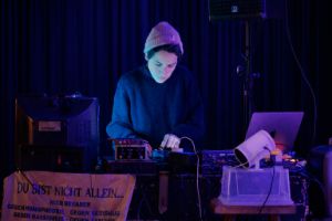 Dafne Narvaez Berlfein at a mixing console. Narvaez Berlfein is wearing a wool hat and a sweater.