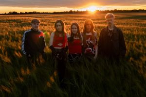 Fünf Personen stehen bei Sonnenuntergang in einem Feld und blicken frontal in die Kamera.