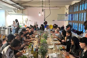 Many people sit at a long wooden table and eat.
