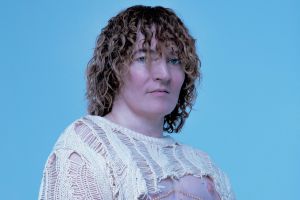 Porträt einer Person mit Locken und einem bauchfreien gestrickten Top.