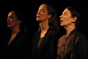 Three people sing with their eyes closed. The lighting is gloomy.