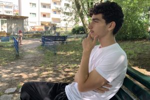 Portrait of Raphaël sitting on a park bench and touching his chin