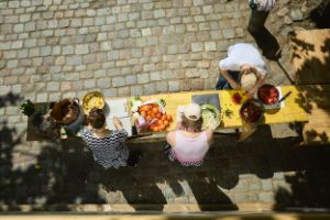 Mitglieder des Internationalen Forum beugen sich in der Sonne über einen Biertisch und schneiden gemeinsam Gemüse.