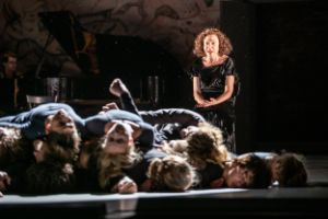 Eine Frau sitzt auf einem Stuhl und schaut auf eine Gruppe übereinanderliegender Körper.