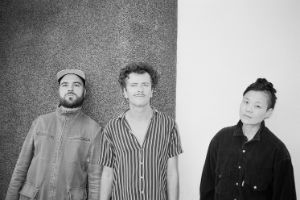 Gruppenfoto des Trios vor einer Wand.