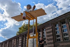 An actress dressed in an astronaut costume sits elevated on a forklift truck.
