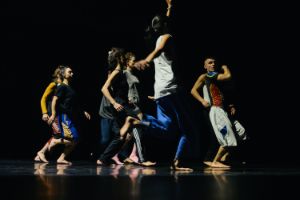 Five dancers striking athletic poses on a dark stage.