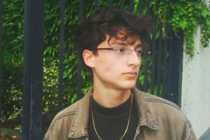 Eine junge Person steht vor grünem Hintergrund und blickt zur Seite.