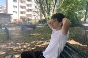 Portrait of Raphaël sitting on a park bench with his arms crossed behind his head