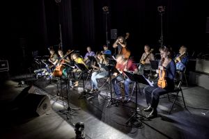 Das Ensemble sitzt in einem Aufführungsraum