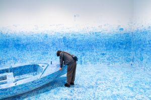 The picture shows a person standing at the bow of a boat in a room painted full of blue colour.