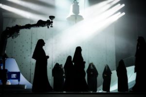 People dressed like nuns stand under a large bell.