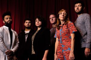 Gruppenfoto des Sextetts, Mary Halvorson trägt einen mit offenen Mündern bedruckten Hosenanzug.