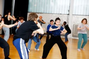 Several people are doing vigorous movement and breathing exercises in a rehearsal room.