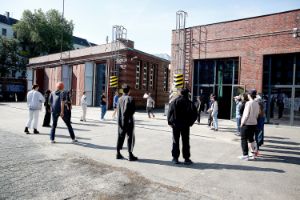 A group of people stand in a circle in front of an old industrial building made of red bricks.