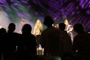 Eine Band auf der Bühne und ein sich bewegendes Publikum davor im Gegenlicht.