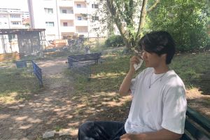 Portrait of Subinn sitting on a park bench with his hand in front of his face