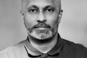 Schwarz-weiß-Porträt: Akram Khan hat eine Glatze und schaut geradeaus in die Kamera.