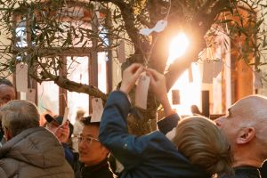Ansicht von Yoko Onos Installation "Wish Tree for Berlin" im Gropius Bau, bei der ein Mann einen kleinen Jungen hochhält, damit dieser einen kleinen Zettel, auf den er einen Wunsch geschrieben hat, an einen Baum im Lichthof des Ausstellungshauses binden kann.