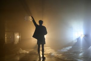 The silhouette of a person with a raised arm is recognisable in a dark room with a transparent film on the floor.