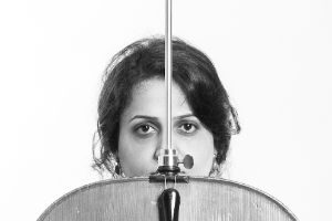 Schwarzweiß Fotografie der Cellistin: Die Hälfte ihres Gesichts wird von ihrem umgekehrten Cello verdeckt.