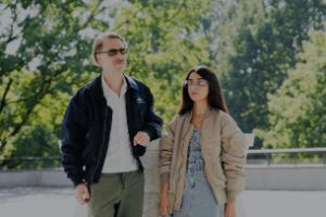 Andrea Belfi and Nazanin Noori leaning on a statue in a sunny and green environment.