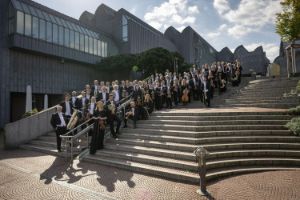 An orchestra stands on the steps behind the Cologne Philharmonic Hall.