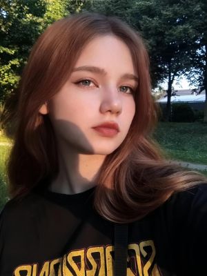 Portraitfotos eines Mädchens, aufgenommen mit der Innenkamera. Sie hat lange braune Haare und trägt ein schwarzes Oberteil mit gelber Aufschrift.