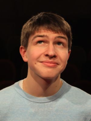 Eine junge Person steht vor schwarzem Hintergrund und schaut lächelnd nach oben.