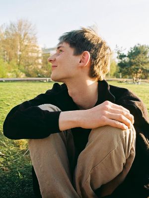 Eine junge Person sitzt auf einer Wiese und schaut lächelnd zur Seite.