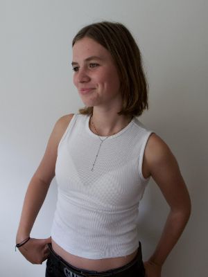 Eine junge Person steht vor einer weißen Wand und blickt lächelnd zur Seite.