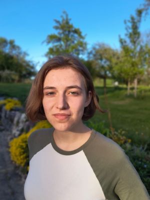 Freya Werner draußen vor Pflanzen. Sie hat halblange Haare und schaut in die Kamera.