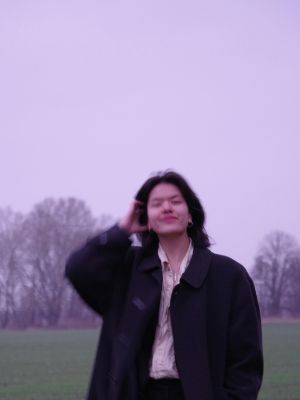 Eine junge Person steht auf einem Feld und blickt lächelnd in die Kamera.