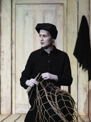 A woman dressed in black and wearing pale make-up sits holding a fishing net.