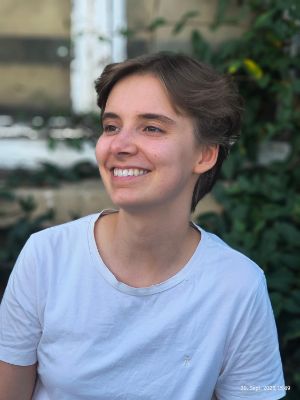 Eine junge Frau blickt lachend zur Seite und trägt ein weißes T-Shirt.