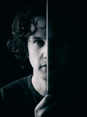 The face of a man looking directly into the camera is shown in black and white. The baton divides his face in two, with the right half being black.