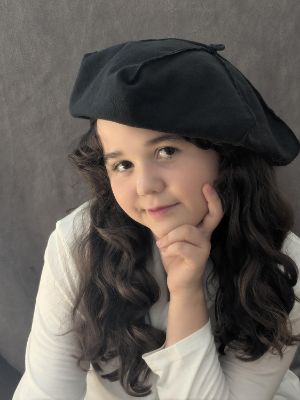 Ein junges Mädchen trägt eine Barrette, stützt ihr Gesicht auf ihrer Hand ab und blickt in die Kamera.