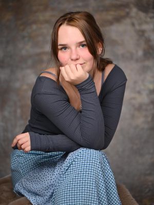 Eine junge Person sitzt nach vorne gelehnt, stützt ihr Gesicht auf ihrer Hand ab und blickt in die Kamera.