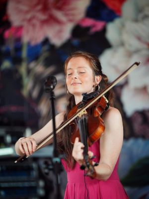Kasia Kapela spielt mit geschlossenen Augen Violine, im Hintergrund ein florales Muster.