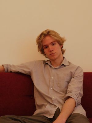 Lennart Kammler sitzt auf einem roten Sofa und schaut in die Kamera.
