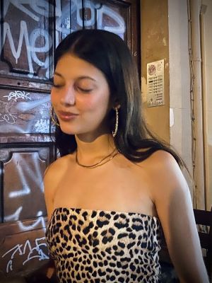 Amelie Singla steht vor einer besprayten Tür und schaut nicht in die Kamera. Sie trägt ein Tigerprint Oberteil.