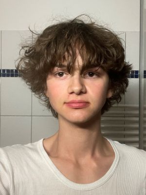 Eine junge Person blickt frontal in die Kamera und trägt ein weißes Shirt.