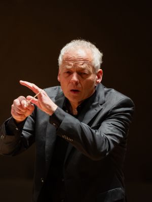 Matthias Hermann beim Dirigieren, im Hintergrund spielt ein Mann Geige.