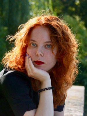 Eine junge Frau stützt ihr Gesicht auf ihrer Hand ab und blickt in die Kamera.