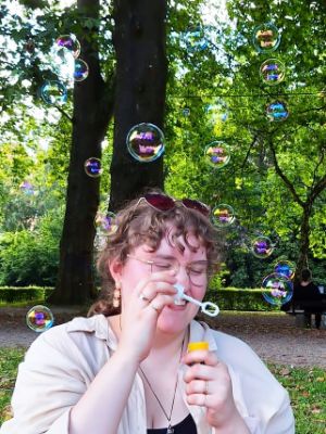 Eine Person im Park pustet Seifenblasen in die Luft.
