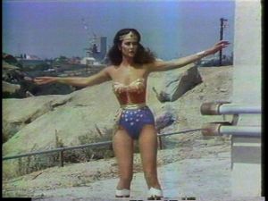 Die Superheldin Wonder Woman der gleichnamigen Serie im Moment ihrer Verwandlung, mit Sternenbanner-Kostüm, wallender Fönfrisur und perfektem Make-up.